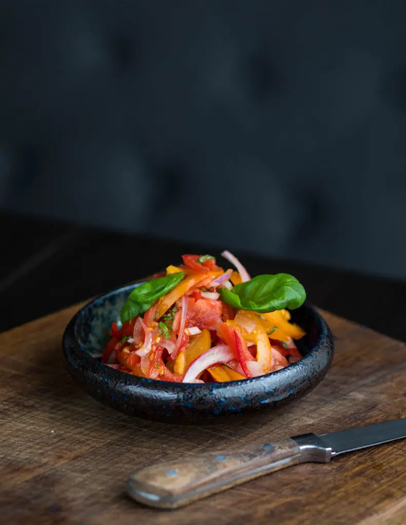 Fresh vegetable salad with colorful peppers and onions in a black bowl on a wooden board.